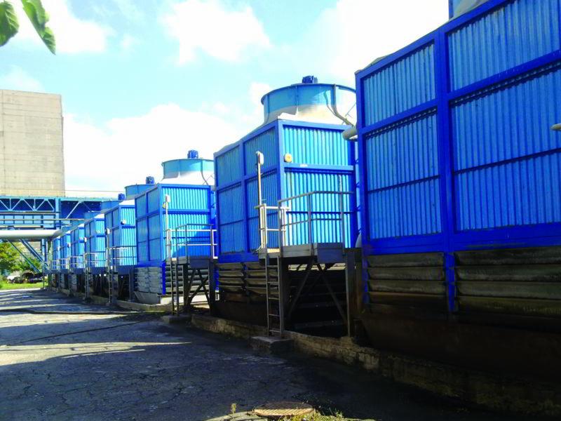 Szereg niebieskich wież chłodniczych z metalowymi drabinkami, widocznych z perspektywy chodnika, z elementami instalacji rurowej w tle.