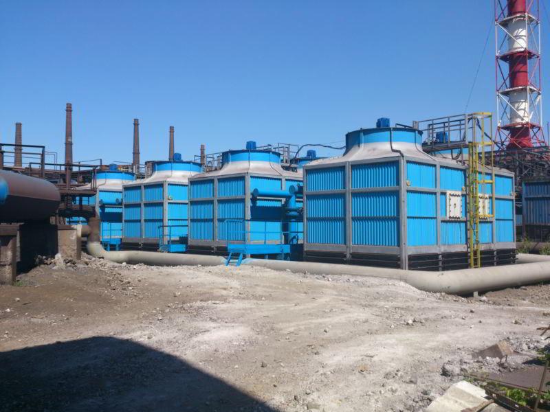 Szereg przemysłowych wież chłodniczych w kolorze niebieskim, ustawionych na zewnątrz, z rurami i kominem w tle.