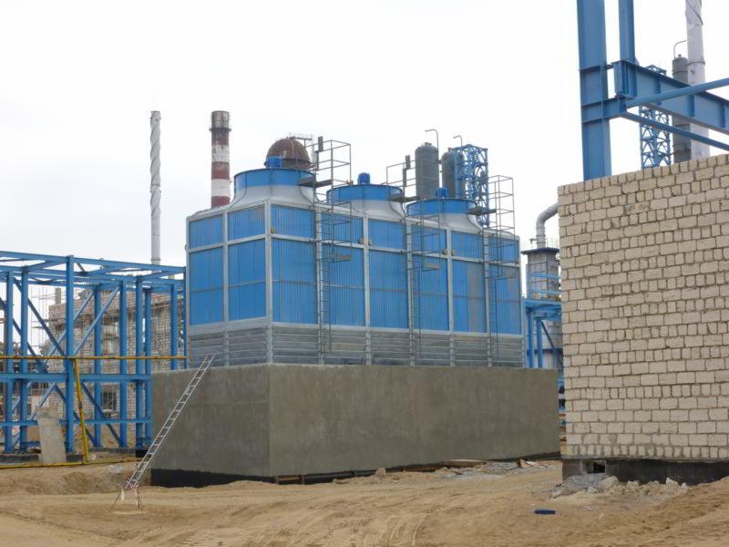 Instalacja przemysłowa chłodnicza z trzema wieżami chłodniczymi z drabinkami, widoczna konstrukcja stalowa i kominy w tle, na placu budowy.