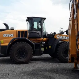 Żółto-czarna ładowarka kołowa Case 821G na żwirowym placu, z rzędem minikoparek i koparko-ładowarek w tle, flaga Case na maszcie.