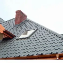 Szary dach z dachówki ceramicznej z oknem dachowym i kominem z cegły w Lwówku Śląskim, widok z dołu.