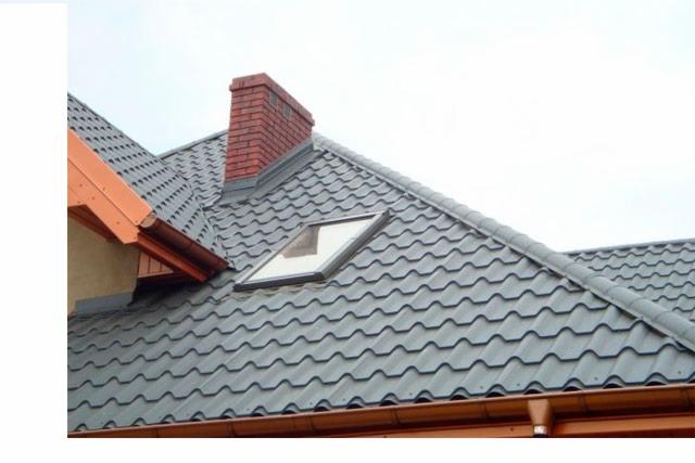 Szary dach z dachówki ceramicznej z oknem dachowym i kominem z cegły w Lwówku Śląskim, widok z dołu.