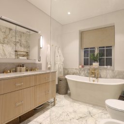 SHARP DESIGN Piotr Golecki - Elegancka łazienka z marmurowymi ścianami i podłogą, wolnostojąca wanna z złotą armaturą, drewniana szafka pod umywalkę z ryflowanymi frontami i lustro z oświetleniem.