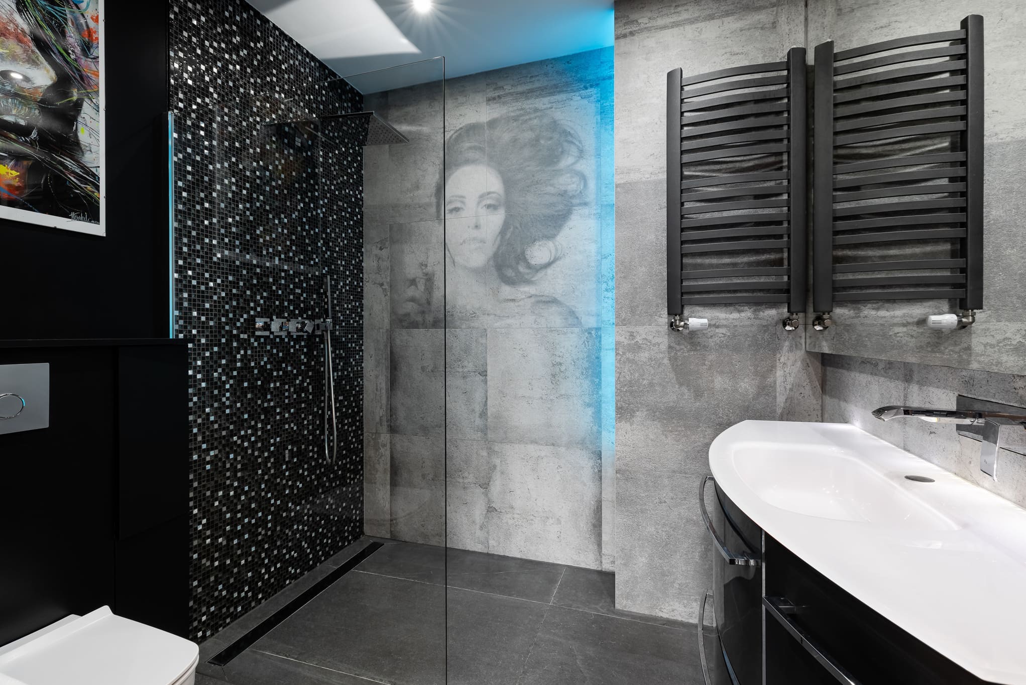 Nowoczesna łazienka z kabiną prysznicową wykończoną mozaiką, szarą armaturą i dekoracyjnym portretem na ścianie. Minimalistyczny design, oświetlenie LED.