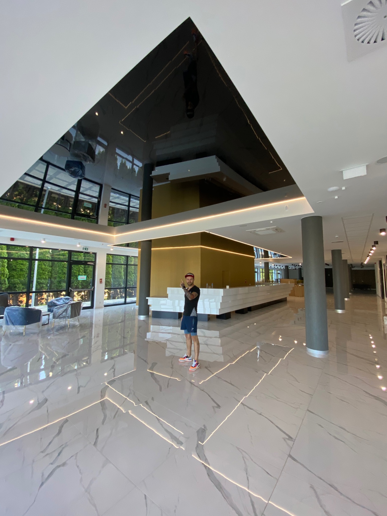 Błyszczący, czarny sufit napinany z refleksami światła w przestronnym holu. Widoczna osoba i marmurowa podłoga.