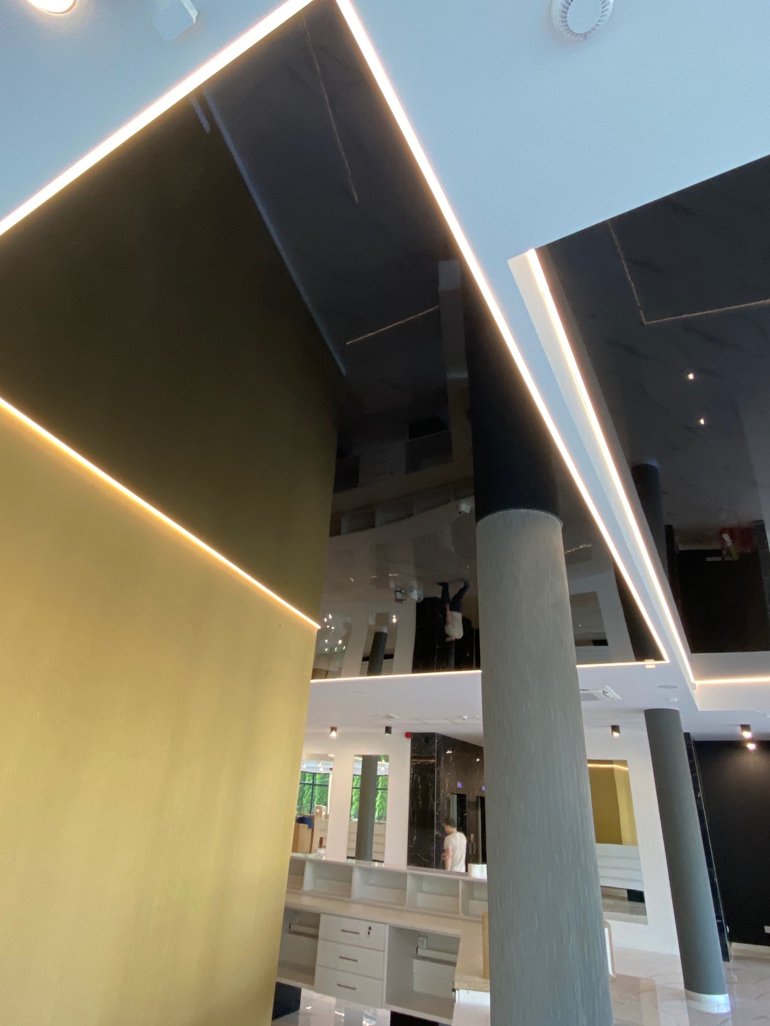 Błyszczący, czarny sufit napinany z oświetleniem LED wzdłuż krawędzi, widok z dołu, kolumny w tle, nowoczesne wnętrze.