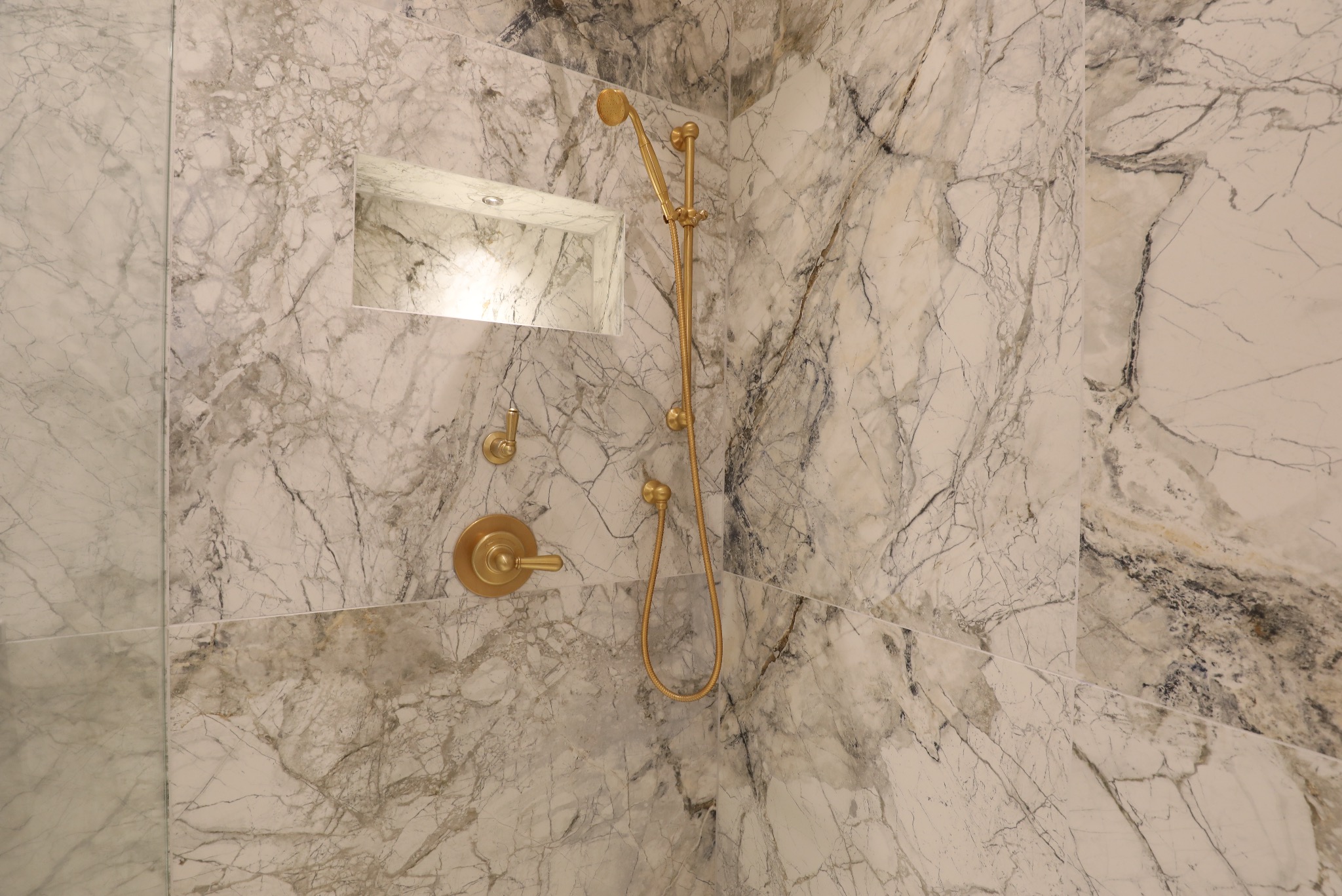 Wykończona łazienka z marmurowymi płytami, złotą armaturą i wnęką z oświetleniem. Nowoczesny design z dbałością o detale.