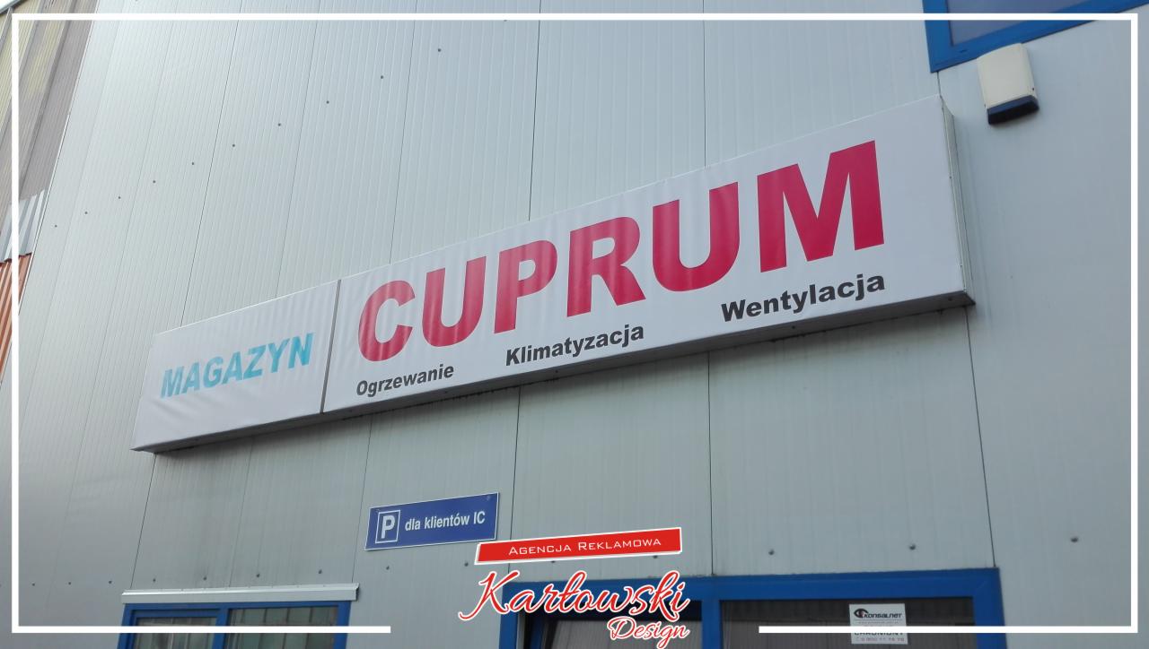 Zewnętrzny szyld reklamowy firmy Cuprum z napisem Magazyn, Ogrzewanie, Klimatyzacja, Wentylacja, umieszczony nad wejściem do budynku o metalowej elewacji.