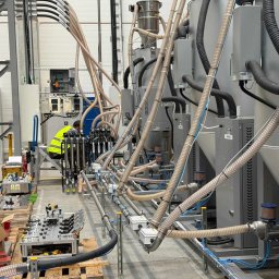 SystemSmart Łukasz Waśniewski - Kompleksowa instalacja przemysłowa z rurami i urządzeniami w hali fabrycznej, widoczny pracownik w kamizelce odblaskowej. Automatyka w fabryce automotive.