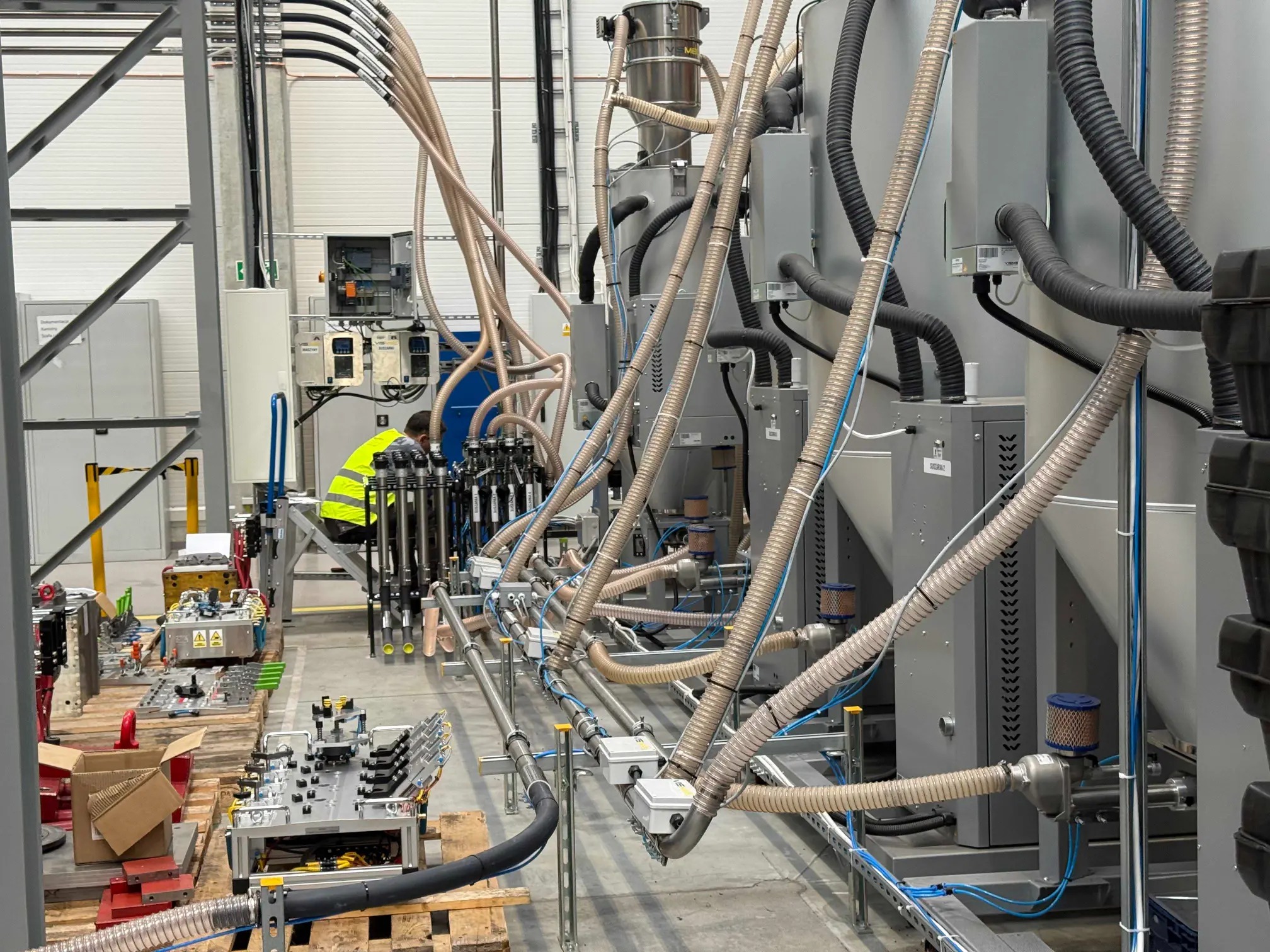 Kompleksowa instalacja przemysłowa z rurami i urządzeniami w hali fabrycznej, widoczny pracownik w kamizelce odblaskowej. Automatyka w fabryce automotive.