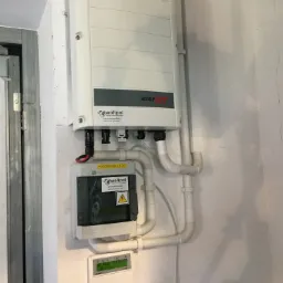 Zamontowany inwerter SolarEdge i rozdzielnica R-DC Woltpol na białej ścianie, widoczne rury instalacyjne i wyświetlacz parametrów. Na inwerterze widoczne logo SolarEdge.