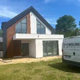 Nowoczesny dom jednorodzinny z elementami drewnianej elewacji w Grudziądzu, widoczny z przodu, z samochodem dostawczym firmy budowlanej w tle.