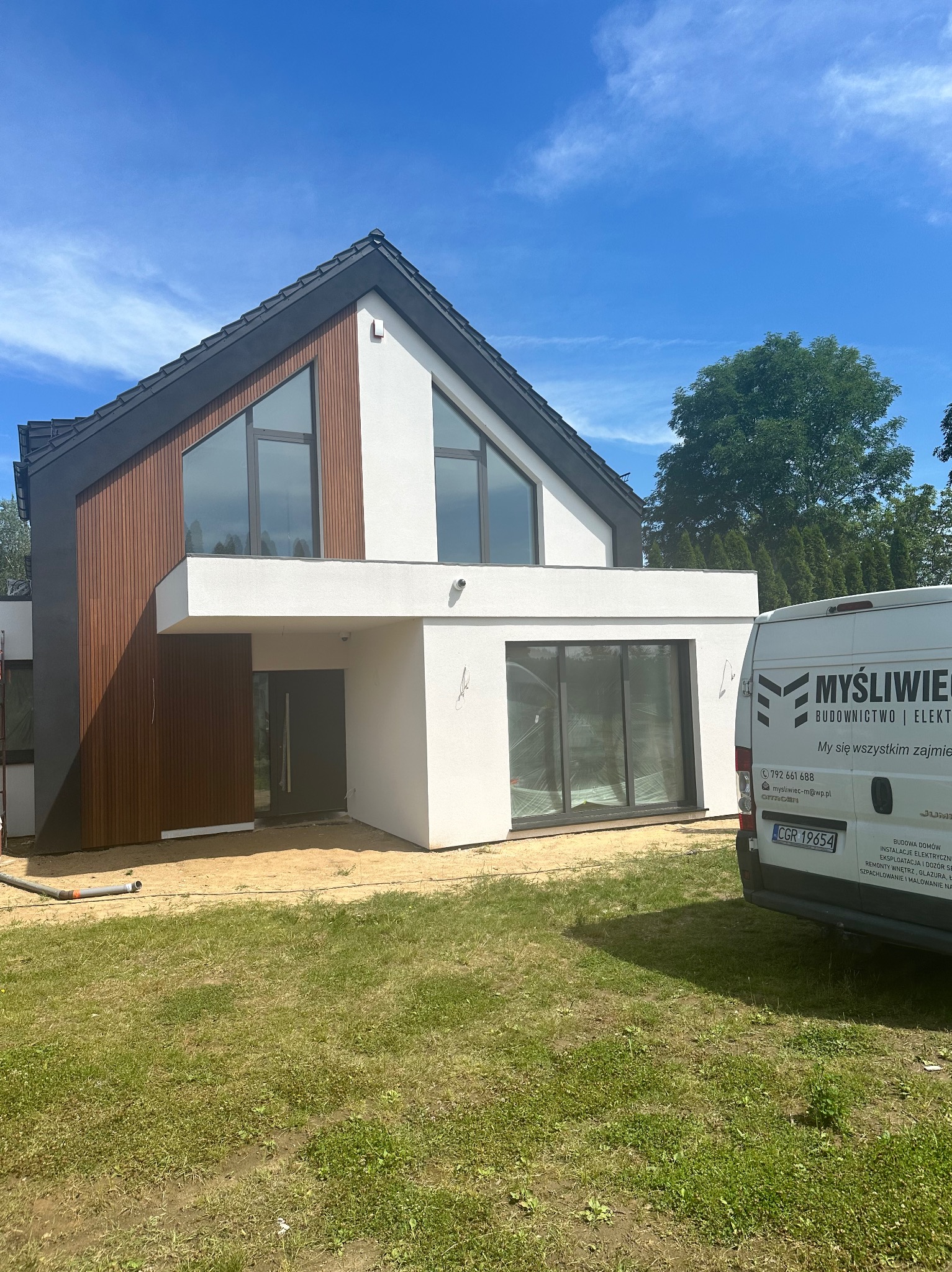 Nowoczesny dom jednorodzinny z elementami drewnianej elewacji w Grudziądzu, widoczny z przodu, z samochodem dostawczym firmy budowlanej w tle.