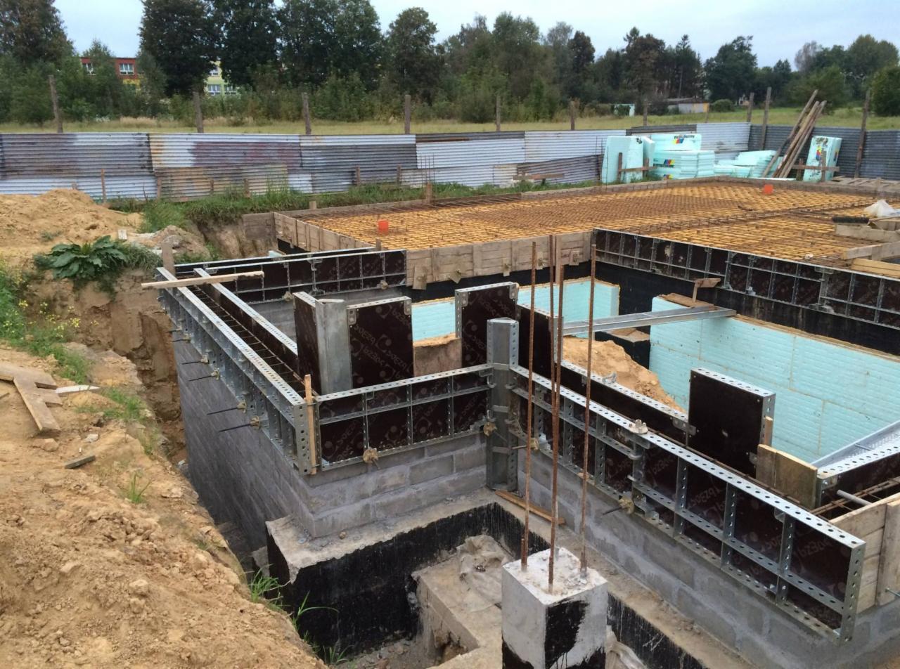 Budowa fundamentów domu: szalunki, zbrojenie, izolacja termiczna ze styropianu, widok z góry na wykop z elementami konstrukcyjnymi.
