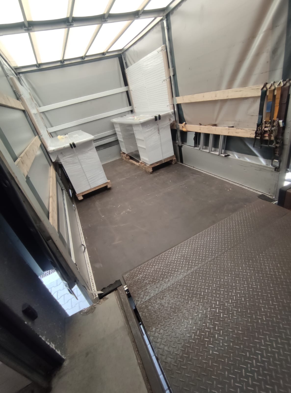 Wnętrze naczepy ciężarówki z ładunkiem zabezpieczonym folią stretch na paletach, widoczne pasy mocujące i drabina oparta o ścianę.