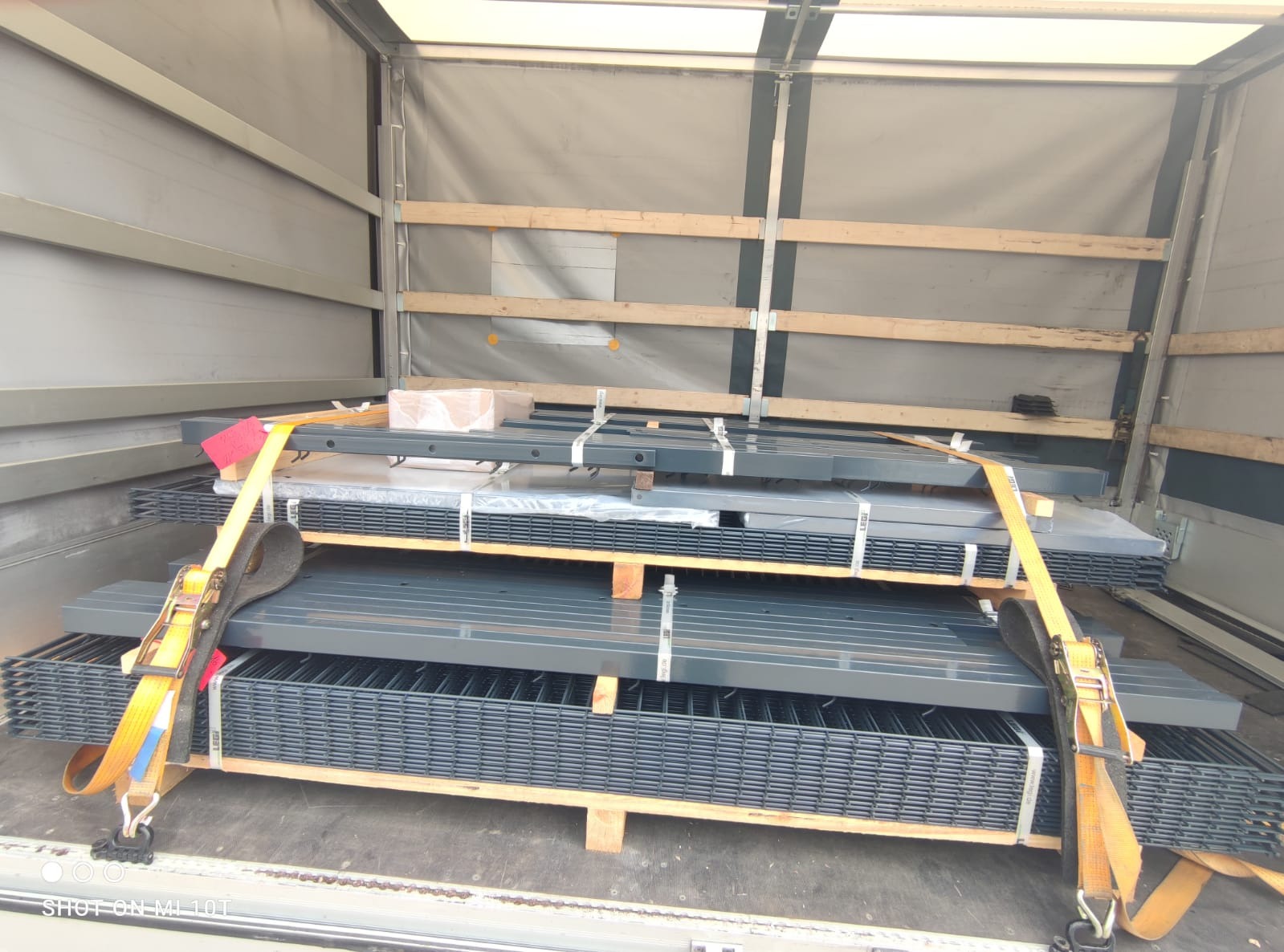 Ładunek metalowych paneli ogrodzeniowych zabezpieczonych pasami transportowymi i drewnianymi przekładkami wewnątrz naczepy ciężarówki.