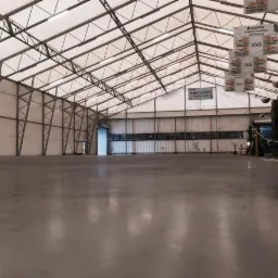 Gładka, szara posadzka przemysłowa w hali magazynowej w Tychach, widok na metalową konstrukcję dachu i ściany, oznaczenia stref składowania.