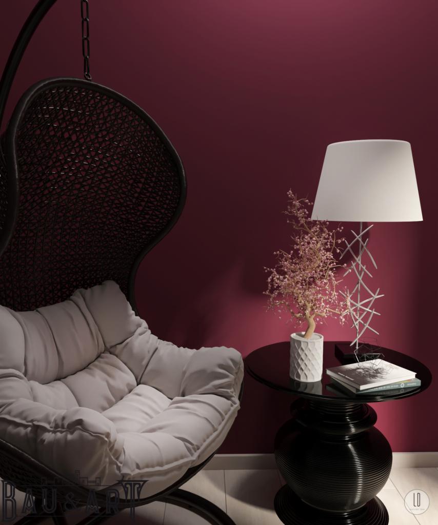 Wnętrze z wiszącym fotelem kokon, małym czarnym stolikiem z dekoracjami: lampą, kwiatem w doniczce i książką na tle bordowej ściany.
