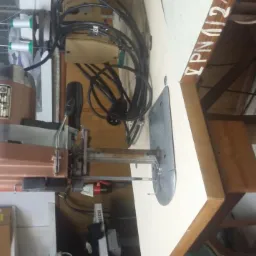 Elektryczna krajalnica krawiecka na stole roboczym, widoczne przewody, silnik i ostrze tnące.