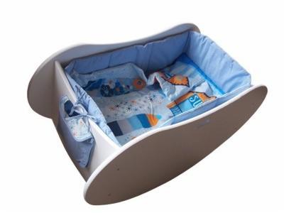 Biała kołyska z niebieską pościelą w dziecięce wzory, widok z góry na białym tle.