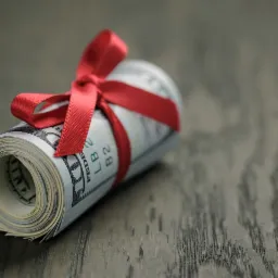 Zwój banknotów dolarowych przewiązany czerwoną wstążką leży na drewnianym blacie. Symbol prezentu finansowego lub oferty specjalnej.
