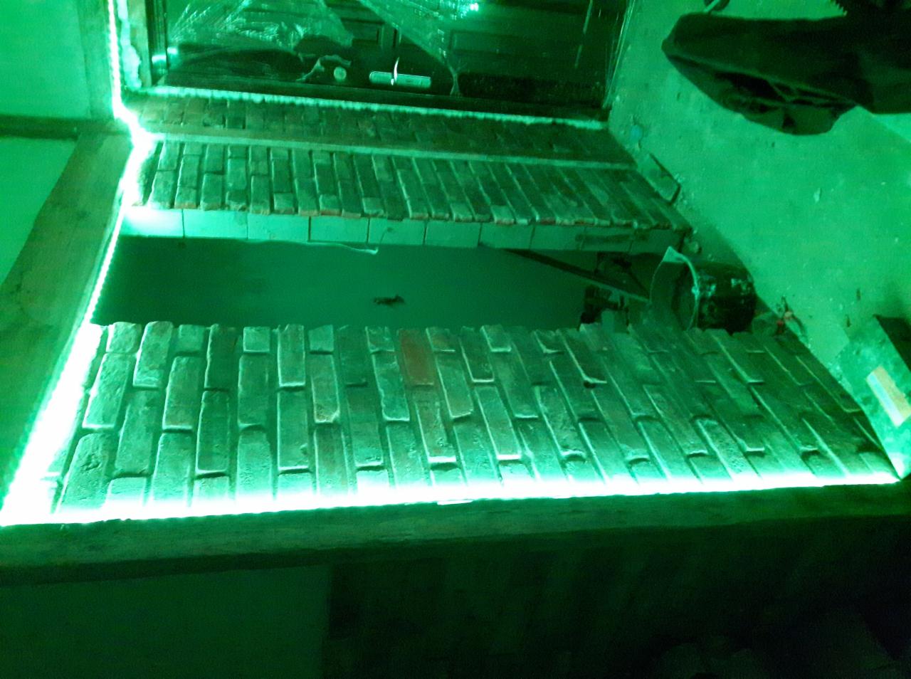 Niedokończona ściana z cegły z podświetleniem LED w zielonym odcieniu, widoczne narzędzia i folia ochronna w tle.