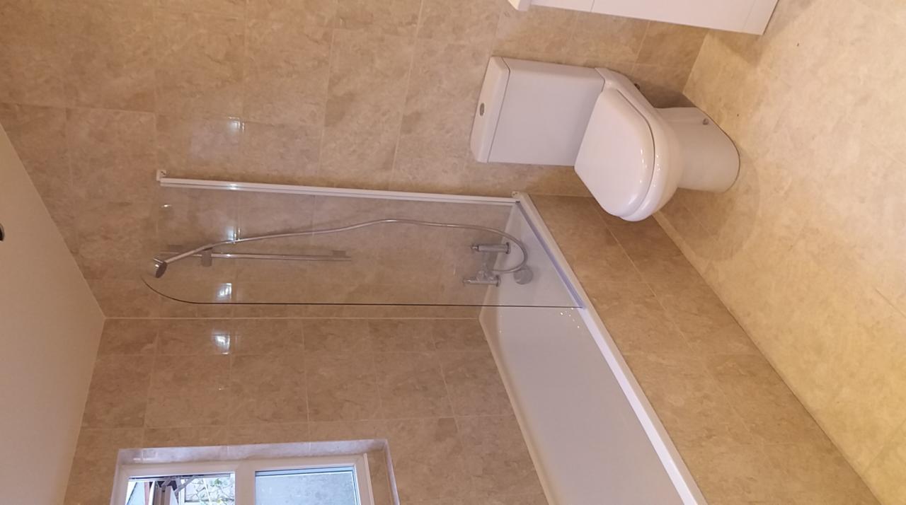 Nowoczesna łazienka z beżowymi płytkami imitującymi marmur, kabiną prysznicową z przezroczystego szkła i białą armaturą, w tym toaletą.