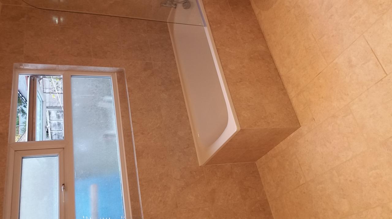 Wykończona łazienka z beżowymi płytkami, białą wanną z zabudową i oknem z widokiem na zewnątrz.