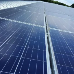 Rząd paneli słonecznych na metalowym dachu, widoczne mocowania i fragment zieleni w tle.