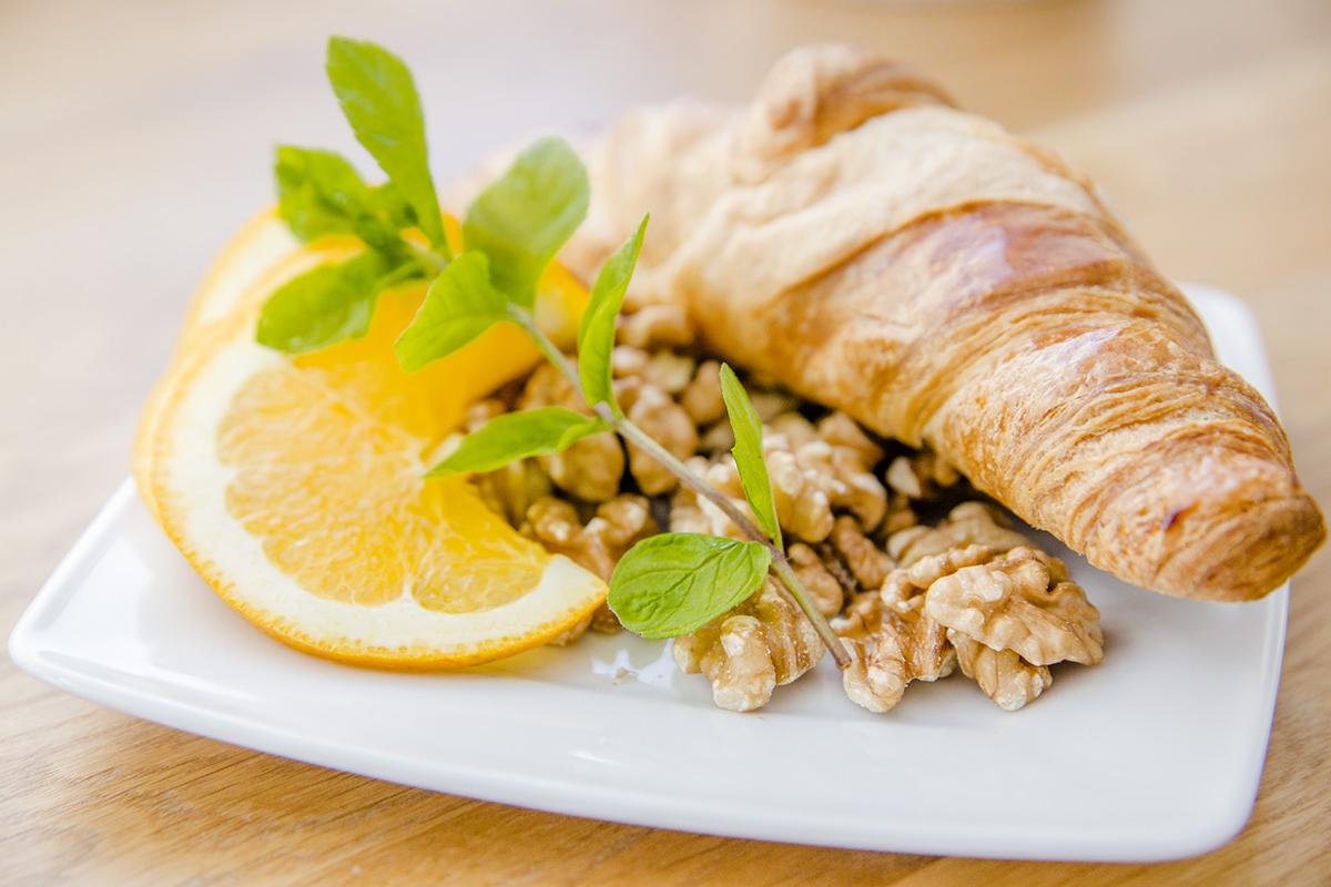 Kruasant z orzechami włoskimi, plasterkiem pomarańczy i gałązką mięty na białym talerzu, serwowany przez catering z Warszawy.