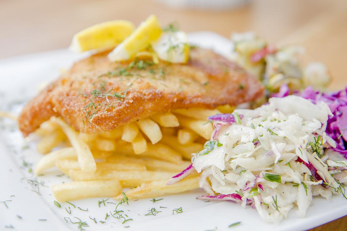 Panierowana ryba z frytkami, udekorowana koperkiem i cytryną, podana z trzema rodzajami sałatek na białym talerzu.