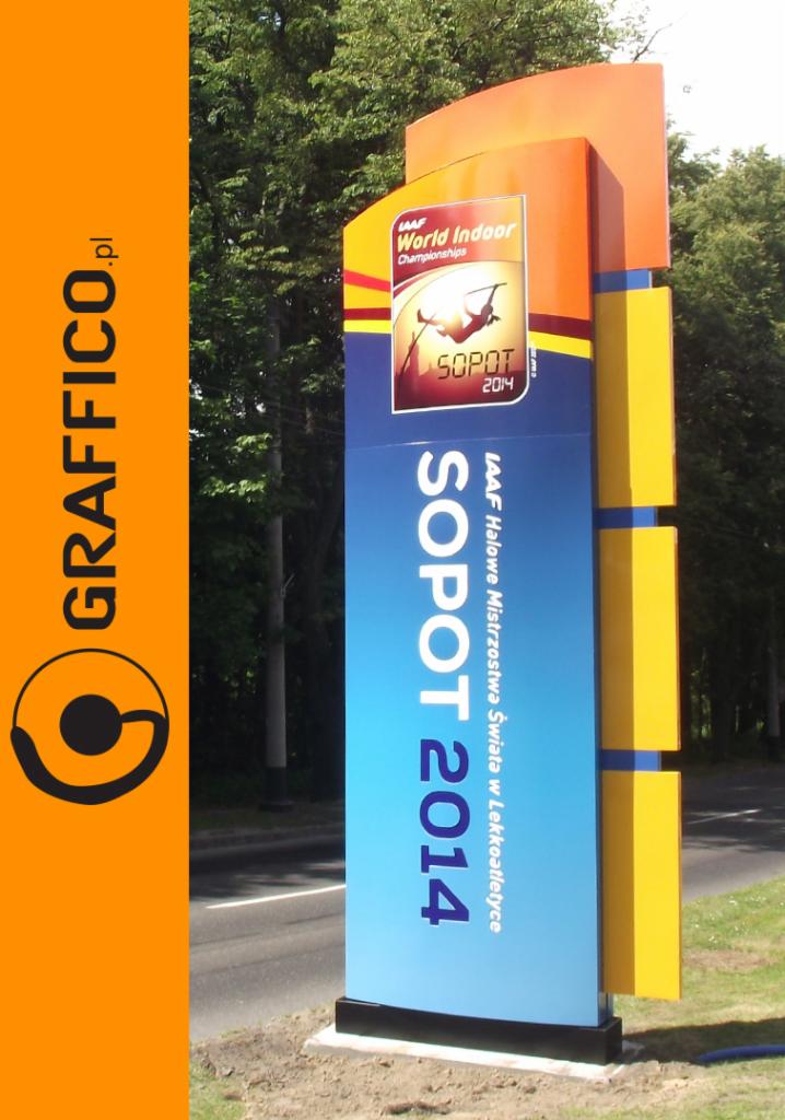 Wieloelementowy, pionowy szyld reklamowy promujący Halowe Mistrzostwa Świata w Lekkoatletyce Sopot 2014, z logo IAAF i sylwetką sportowca, obok pionowy panel z logo firmy Graffico.pl