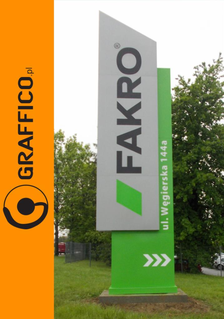 Pylon reklamowy z logo firmy FAKRO i adresem ul. Węgierska 144a, obok pionowy szyld z logo firmy GRAFFICO w kolorze pomarańczowym, na tle zieleni drzew i trawnika.