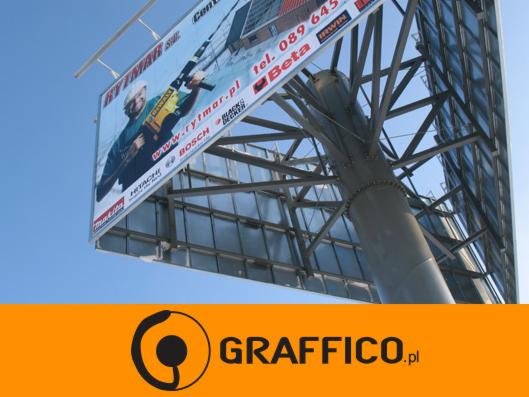 Billboard reklamowy z mężczyzną używającym wiertarki udarowej, widoczny z dołu na tle błękitnego nieba, z fragmentem logotypu firmy GRAFFICO.pl w dolnej części.