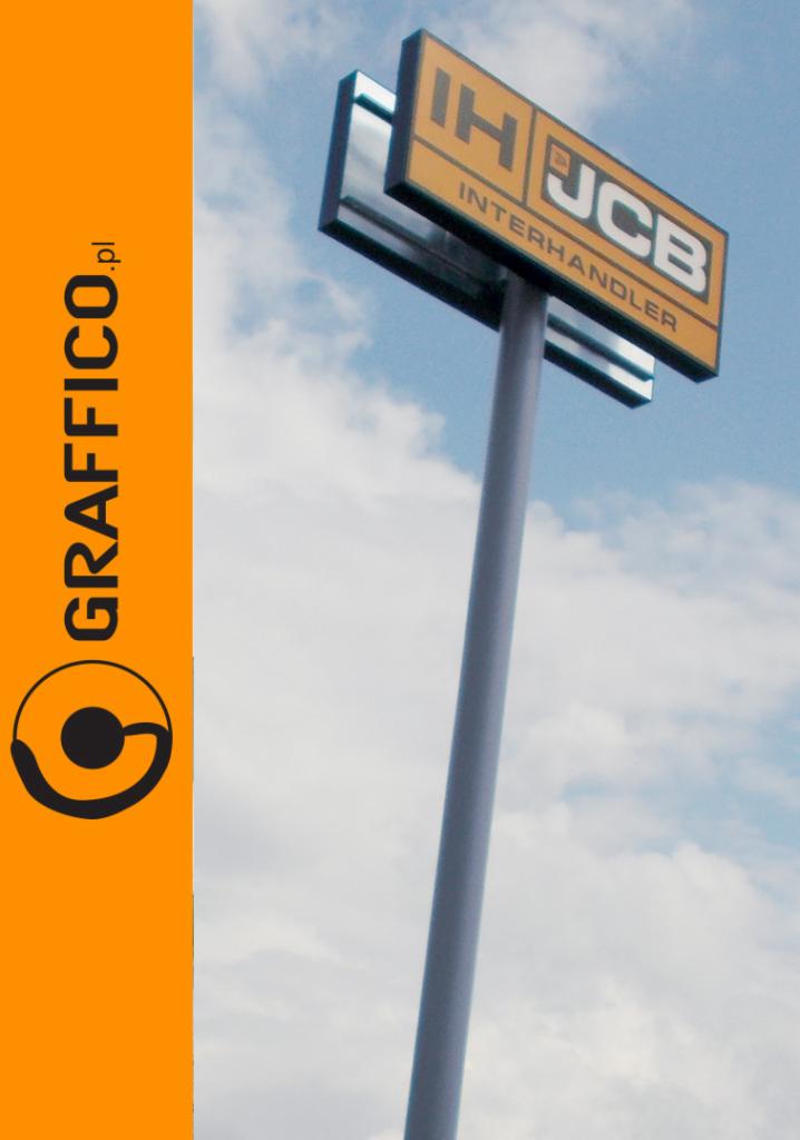 Pylon reklamowy z logo IH JCB Interhandler na tle błękitnego nieba, z pionowym logo Graffico.pl po lewej stronie.