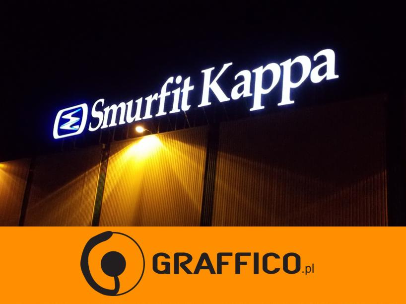 Podświetlany szyld firmy Smurfit Kappa na ciemnym tle budynku, oświetlony dodatkowo lampą uliczną, widoczny znak firmowy Graffico.pl