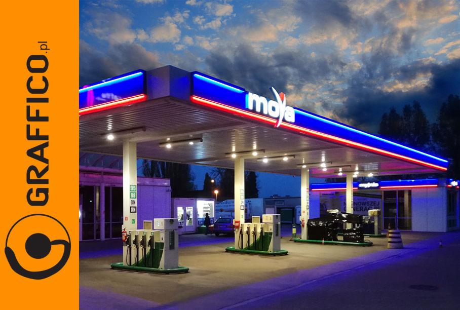 Stacja benzynowa Moya z podświetlanym logo i neonami pod zadaszeniem, widoczna wieczorową porą z logo GRAFFICO.pl po lewej stronie.