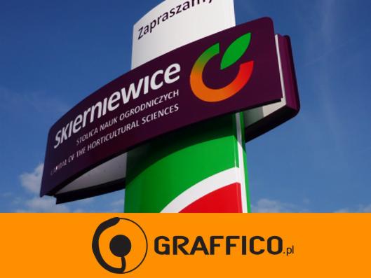 Tablica informacyjna z logo i nazwą miejscowości Skierniewice, stolica nauk ogrodniczych, na tle błękitnego nieba.