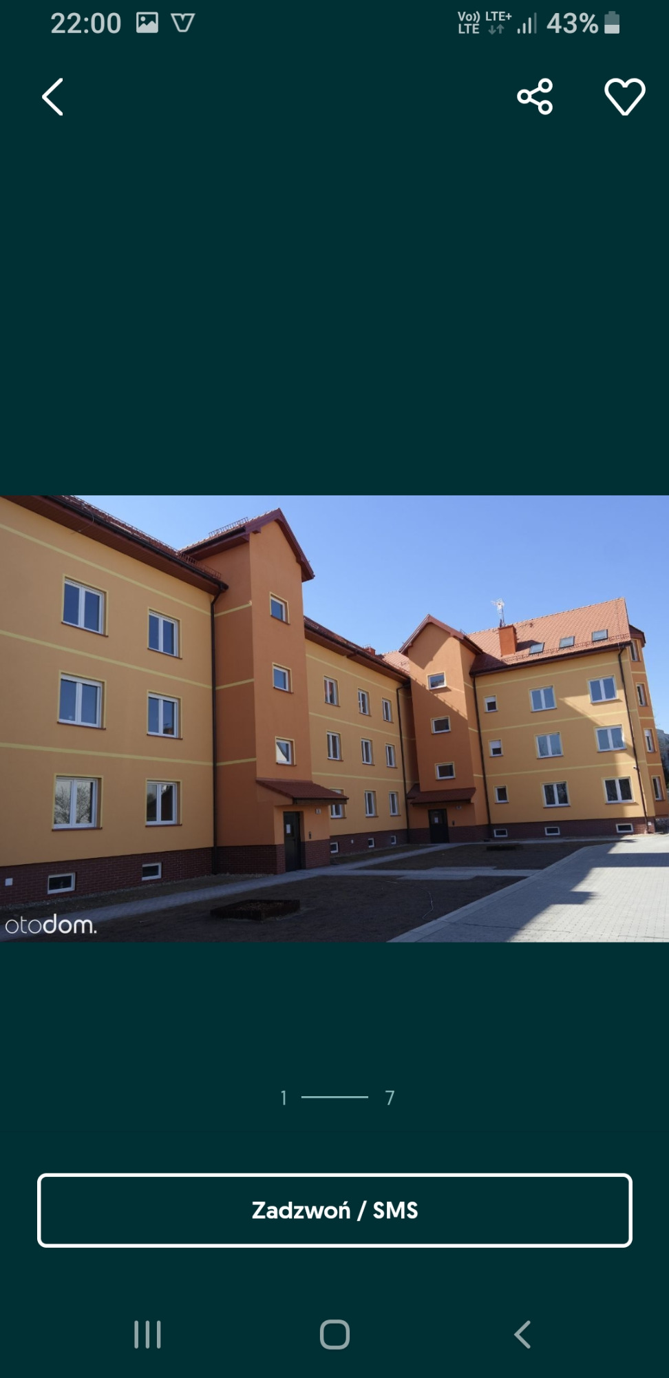 Nowo wybudowany, trzypiętrowy budynek mieszkalny z pomarańczową elewacją i brązowymi akcentami architektonicznymi, widoczny z poziomu chodnika.