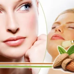 Kobieta z jasną cerą i niebieskimi oczami, obok zabieg z użyciem pędzla na twarzy innej kobiety z ręcznikiem na głowie, migdały w tle.