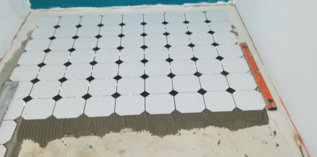 Układanie podłogi z białych, ośmiokątnych płytek z czarnymi wstawkami w Skoczowie, widoczny pasek kleju i poziomica