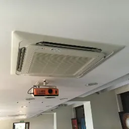 Kasetonowa jednostka klimatyzacji LG zamontowana w suficie podwieszanym, widoczny także pomarańczowy projektor przymocowany do sufitu.