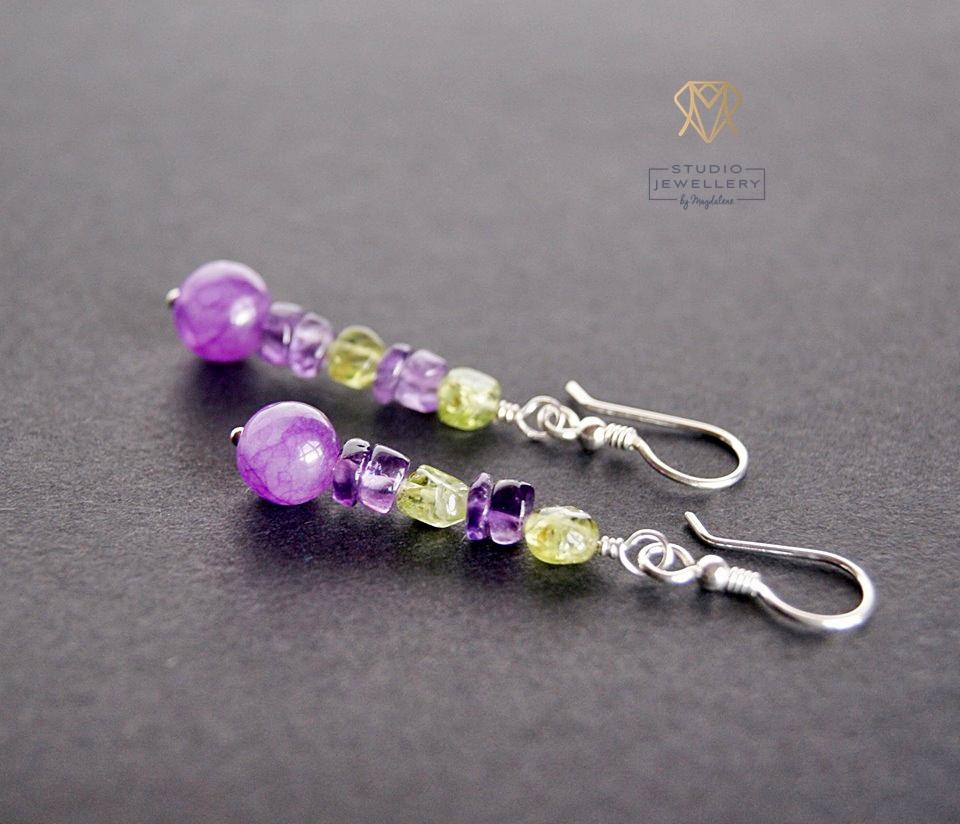 Dwa srebrne kolczyki z fasetowanymi kulkami z ametystu i oliwinu na szarym tle, z logo 'Studio Jewellery by Magdalena' w prawym górnym rogu.