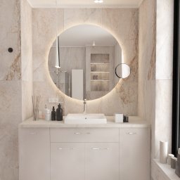 AZArchitekci Pracownia Architektury Wnętrz - Nowoczesna łazienka z marmurowymi ścianami, okrągłym lustrem z podświetleniem LED, białą szafką pod umywalką i minimalistycznymi akcesoriami.