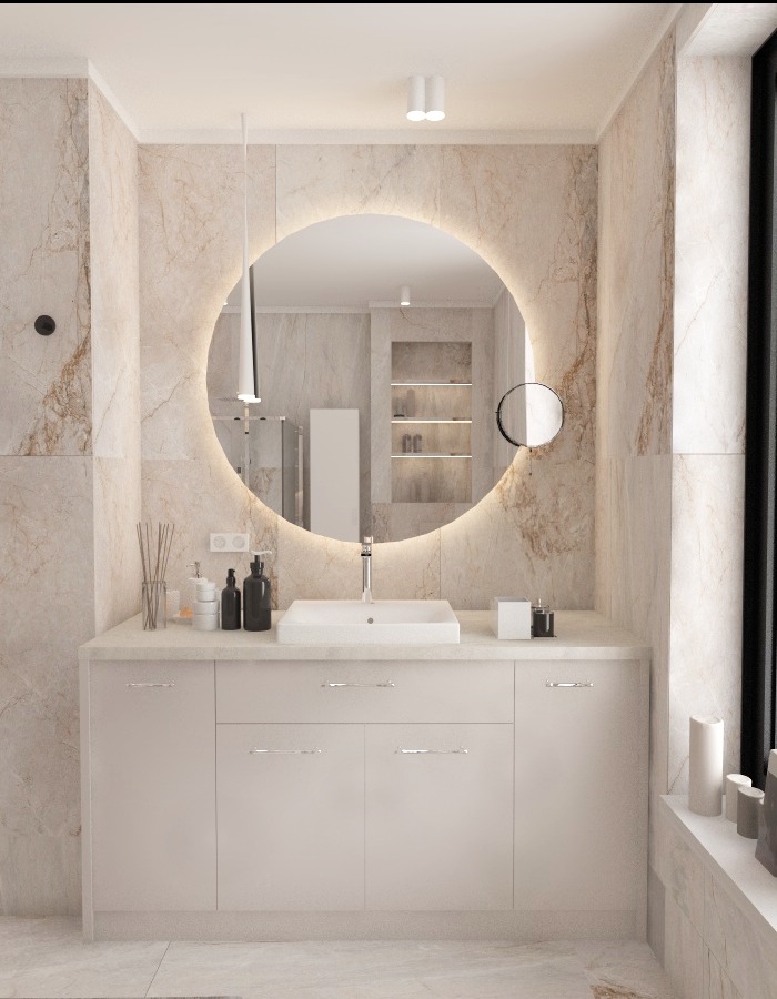 Nowoczesna łazienka z marmurowymi ścianami, okrągłym lustrem z podświetleniem LED, białą szafką pod umywalką i minimalistycznymi akcesoriami.
