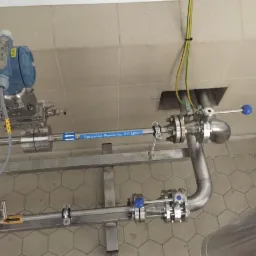 Instalacja rur ze stali nierdzewnej z zaworami kulowymi i manometrem, oznaczona etykietą 'Sprężone Powietrze 0.6 MPa', widoczne przewody elektryczne i fragment kafelkowanej ściany.