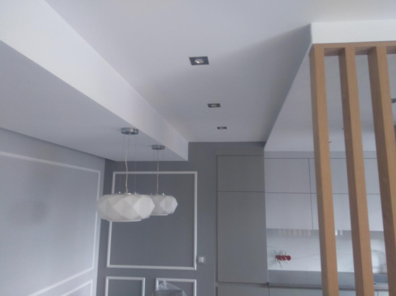 Nowoczesne wnętrze w Wodzisławiu Śląskim z szarą ścianą ozdobioną sztukaterią, białym sufitem z oświetleniem punktowym i wiszącymi lampami o geometrycznym kształcie oraz drewnianą ażurową ścianką...