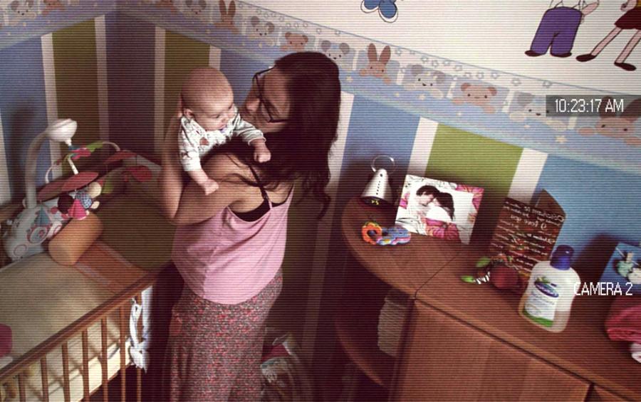 Kadr z kamery monitoringu: kobieta trzyma niemowlę w pokoju dziecięcym z łóżeczkiem i zabawkami, widoczny datownik 10:23:17 AM.