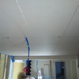 Montaż sufitu podwieszanego z płyt gipsowo-kartonowych z instalacją elektryczną i rurami wentylacyjnymi przed szpachlowaniem.