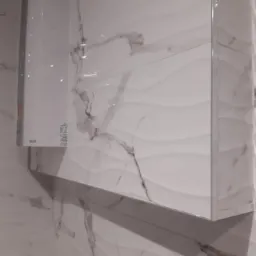 Biała, marmurkowa glazura ścienna z dekoracyjnym wzorem fal, z zamontowanym białym szafką łazienkową z połyskiem i chromowanymi krawędziami.